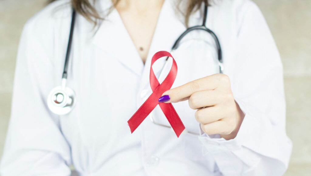 A healthcare professional in a white coat holding a red ribbon, the global symbol for HIV/AIDS awareness and support.