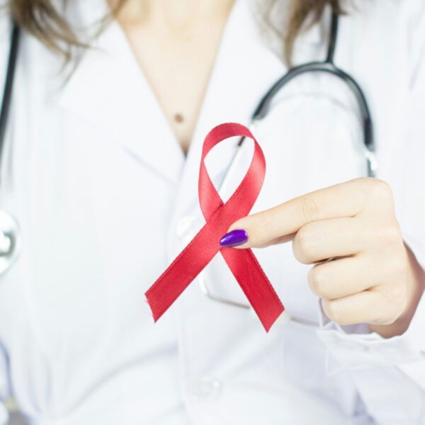 A healthcare professional in a white coat holding a red ribbon, symbolizing the AL HIV/AIDS crisis and availability of medical cannabis for HIV wasting syndrome in Alabama