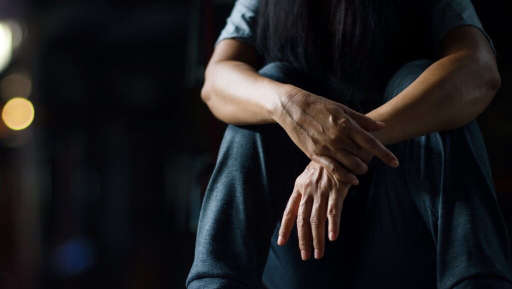 Conceptual photo of a man sitting alone in a dark room representing the isolation, hyperarousal, and sleep anxiety associated with PTSD.