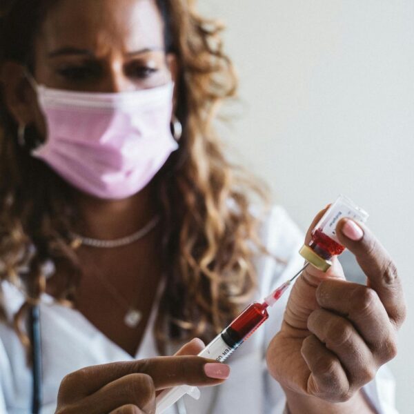 A medical doctor in a clinical setting drawing a blood sample using a needle and injecting it into a vial for sickle cell anemia testing.