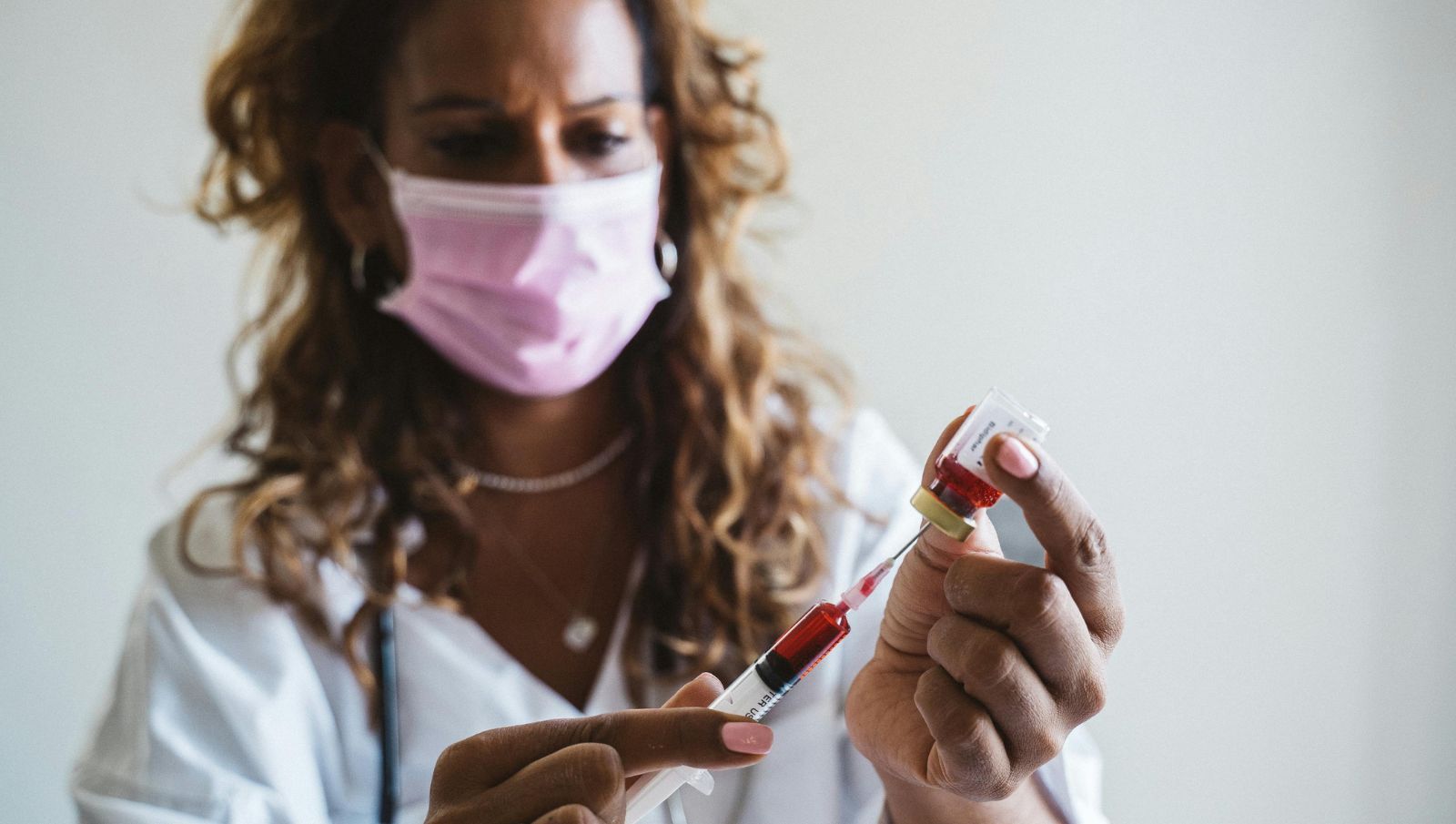 A medical doctor in a clinical setting drawing a blood sample using a needle and injecting it into a vial for sickle cell anemia testing.