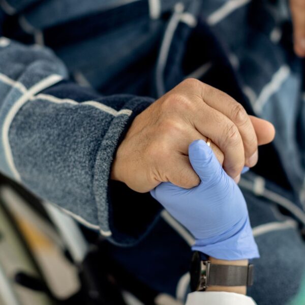 An elderly man in a wheelchair holding the hand of his caregiver, representing medical cannabis support for Alabama residents with ALS, MS, and spinal cord injuries.