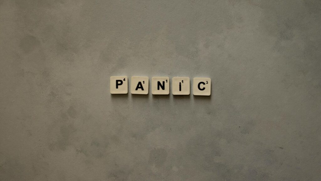 The word Panic spelled out in vintage wooden blocks on a flat surface against a solid black background to show the isolating feeling of anxiety.