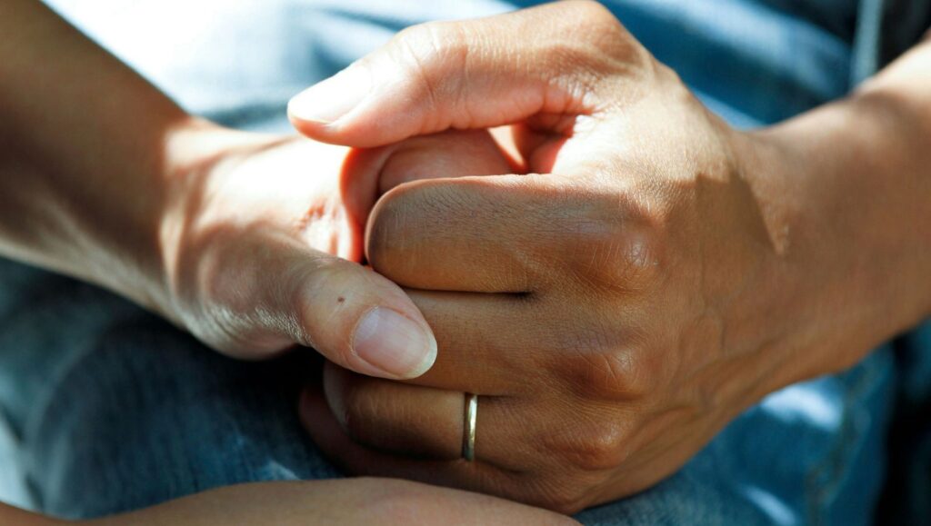 Close-up of two people holding hands, representing patient and caregiver support