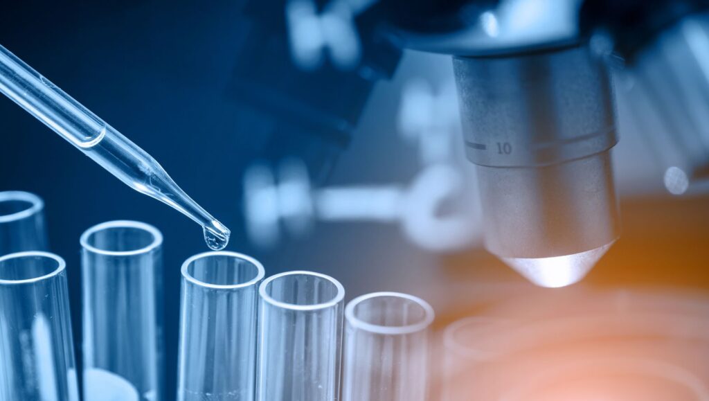 Close-up of a dropper adding liquid to a vial beside a microscope during cannabinoid laboratory testing