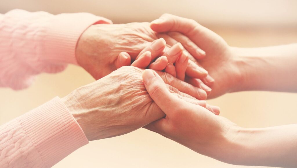 Close-up of a caregiver's hands holding a patient's hands, representing trusted caregiver support