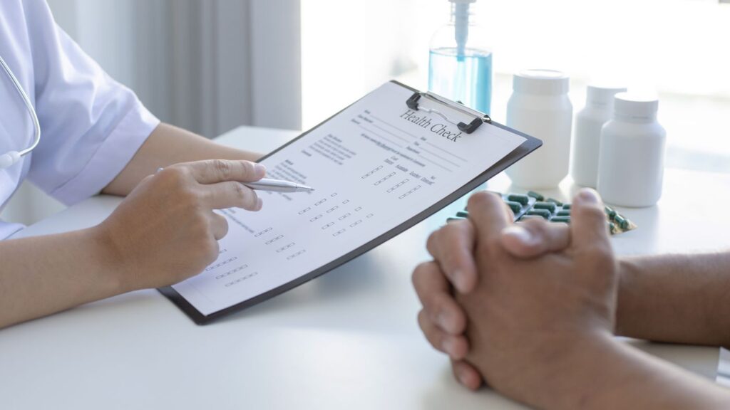 Close-up of an Alabama certifying physician reviewing patient health records and medical charts on a clip board and tablet at a desk.