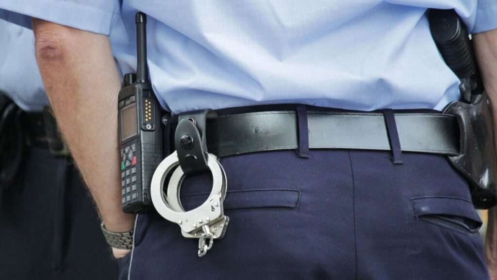 Close-up of metallic steel police handcuffs resting on a officer's dark utility belt loop.