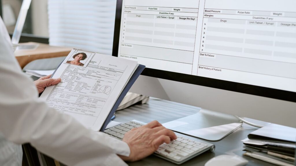A doctor typing confidential health information into a computer database at an office desk.