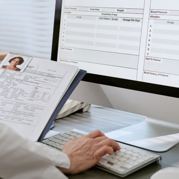 A doctor typing confidential health information into a computer database at an office desk.