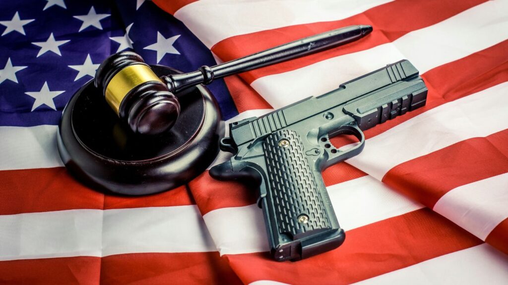 A handgun and a wooden judge's gavel resting on top of an American flag.