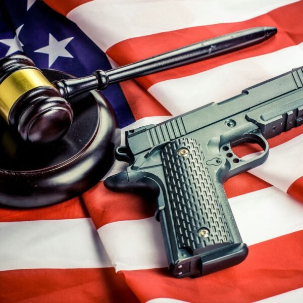 A handgun and a wooden judge's gavel resting on top of an American flag.