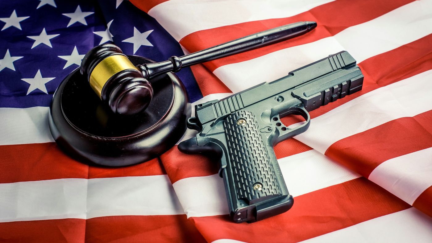A handgun and a wooden judge's gavel resting on top of an American flag.